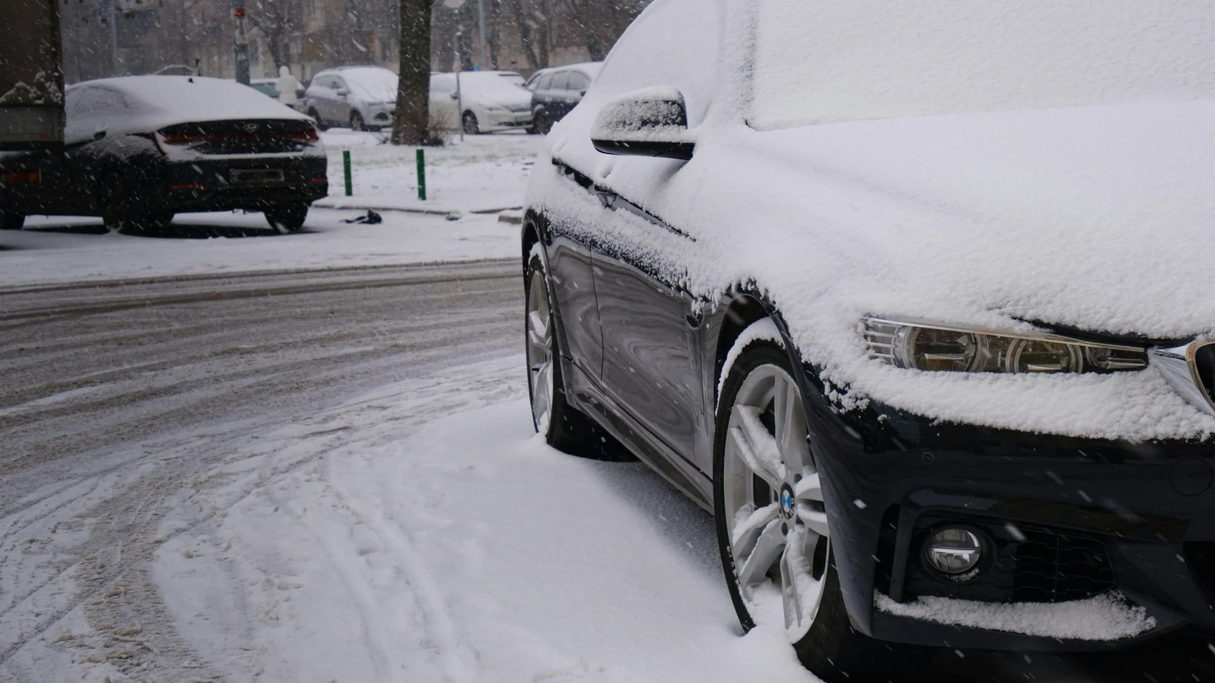 Schwarzer BMW unter einer dichten Schneeschicht am Straßenrand, Streusalz und Schneematsch auf der Fahrbahn
