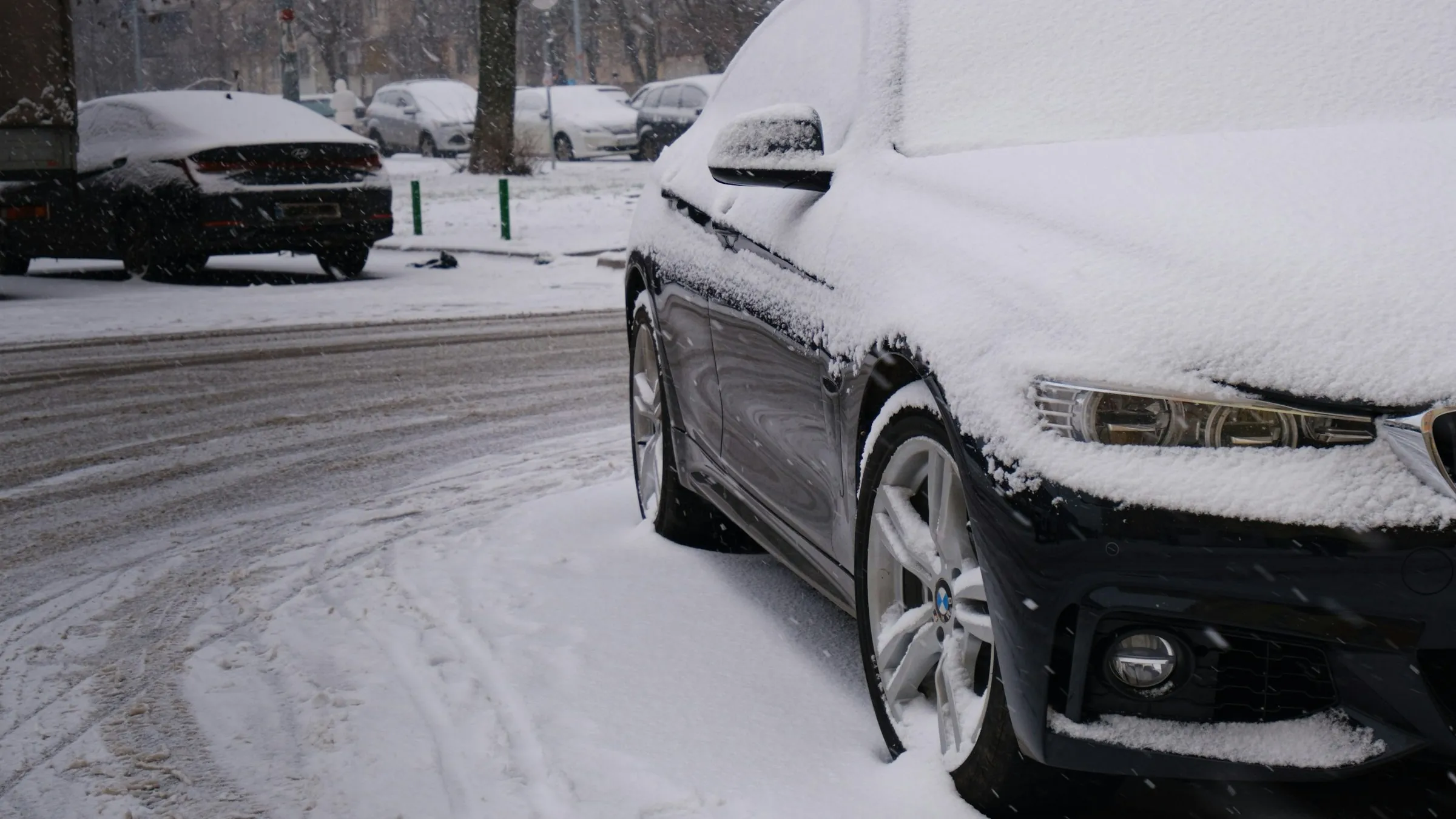 Schwarzer BMW unter einer dichten Schneeschicht am Straßenrand, Streusalz und Schneematsch auf der Fahrbahn